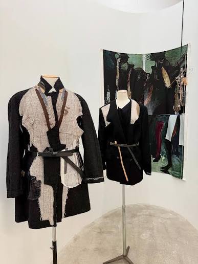 Two belted coats on mannequins; the left one carries pale patchwork panels stitched over dark wool.