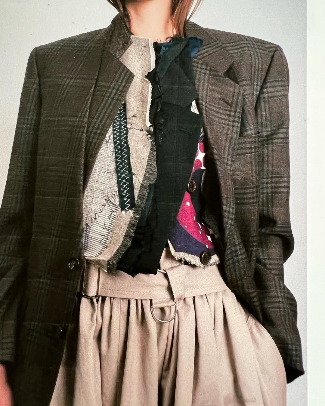 A checked wool jacket worn open over a bodice pieced together from raw-edged patches, joined with visible zigzag hand stitching.