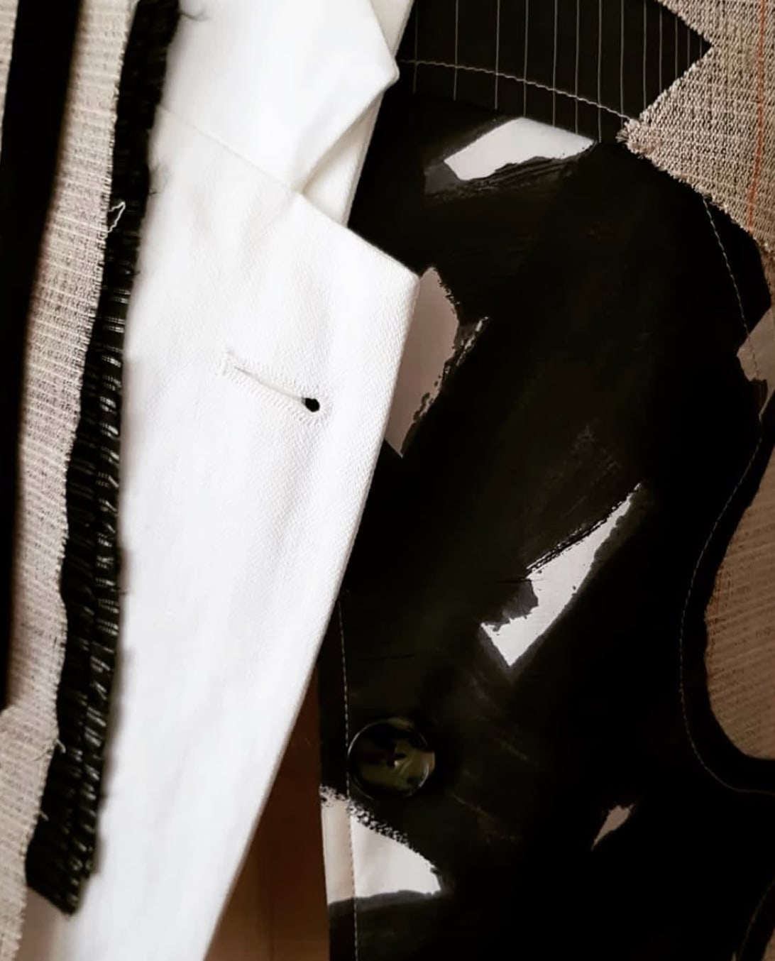 A white lapel against black fabric painted over in broad strokes, a row of dark stitches down its edge.