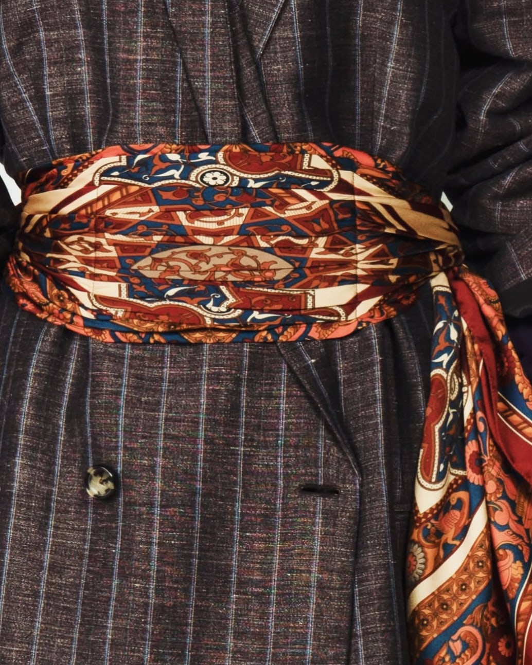 A pinstriped coat tied at the waist with a patterned silk scarf in rust and blue.