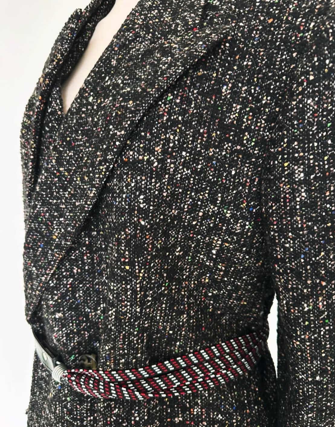 A flecked tweed jacket cinched with a narrow woven belt in red and blue.