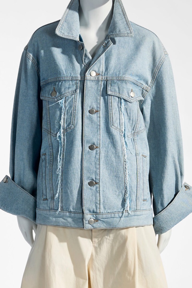 A pale, oversized denim jacket on a mannequin, the cuffs turned back and threads hanging loose down the front.